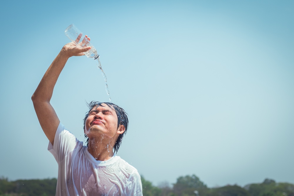Young man pouring water to cool his head
