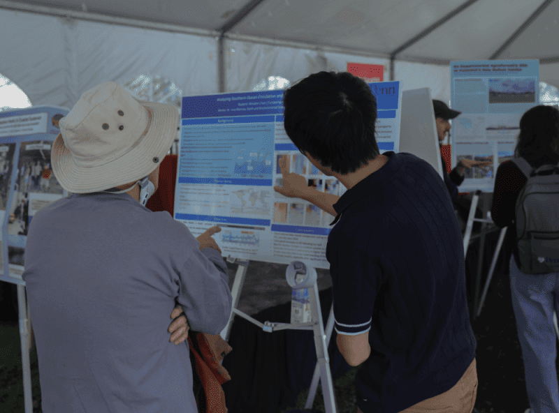 The image shows a person pointing at their research poster underneath the climate week tent.
